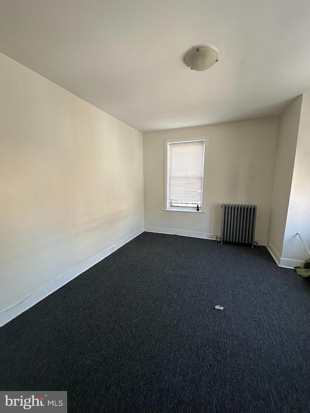 unfurnished room featuring radiator heating unit and dark carpet