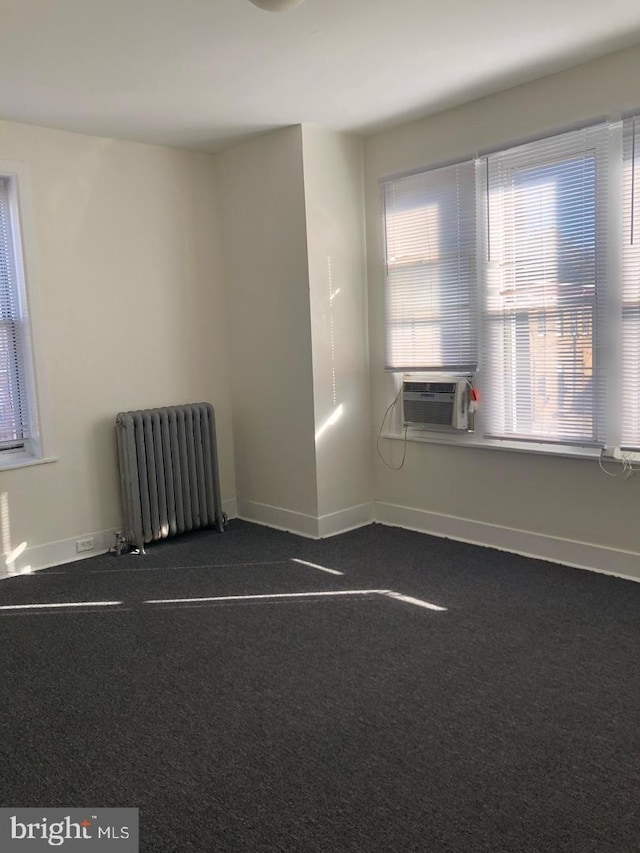 unfurnished room with dark colored carpet, cooling unit, and radiator