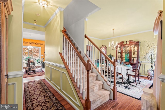 stairway featuring crown molding, wood-type flooring, and an inviting chandelier