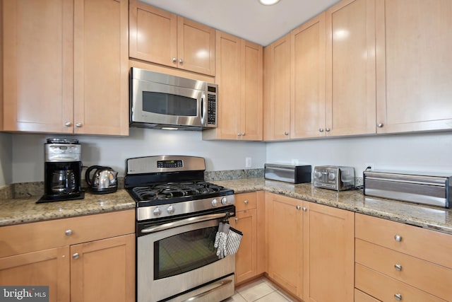 kitchen featuring light brown cabinets, light tile patterned floors, stainless steel appliances, and light stone counters