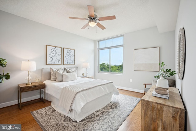 bedroom with ceiling fan, light wood-type flooring, and a textured ceiling