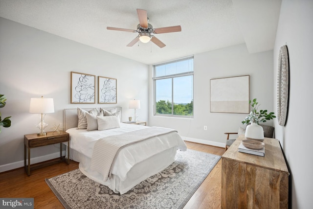 bedroom with ceiling fan, wood-type flooring, and a textured ceiling