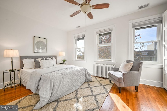 bedroom featuring hardwood / wood-style flooring, ceiling fan, radiator heating unit, and multiple windows