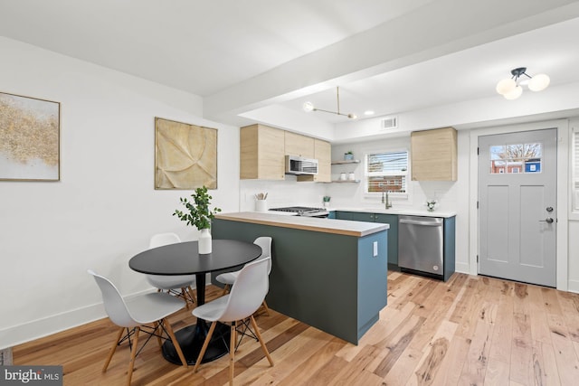 kitchen with light brown cabinets, kitchen peninsula, a chandelier, light hardwood / wood-style floors, and appliances with stainless steel finishes