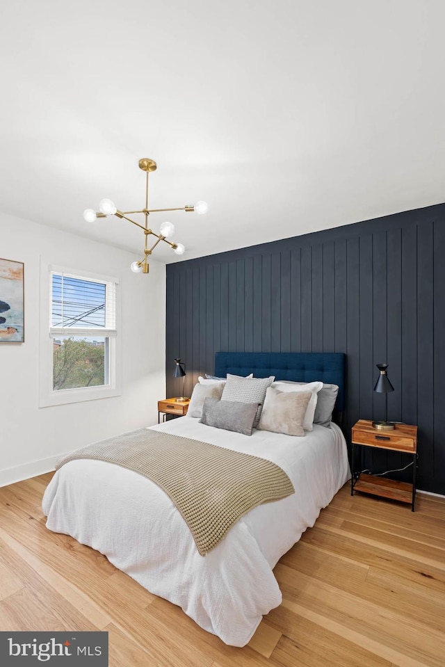 bedroom with light hardwood / wood-style floors, an inviting chandelier, and wood walls