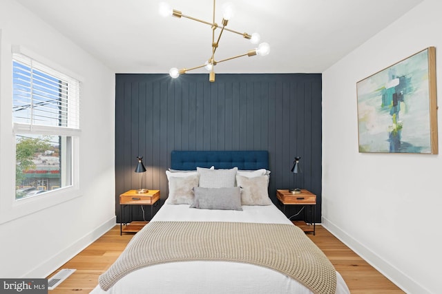 bedroom featuring a notable chandelier, wood walls, and wood-type flooring