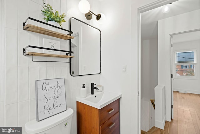 bathroom featuring vanity, toilet, wood-type flooring, and tile walls