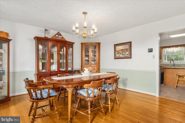 dining area featuring a textured ceiling, light hardwood / wood-style floors, sink, and a chandelier