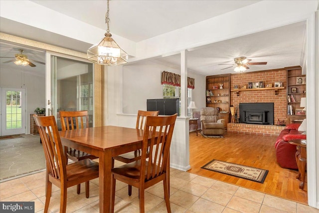 dining area with built in shelves, a wood stove, crown molding, light tile patterned floors, and ceiling fan with notable chandelier