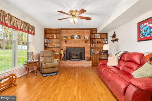 living room with a wood stove, ceiling fan, built in shelves, light wood-type flooring, and a textured ceiling