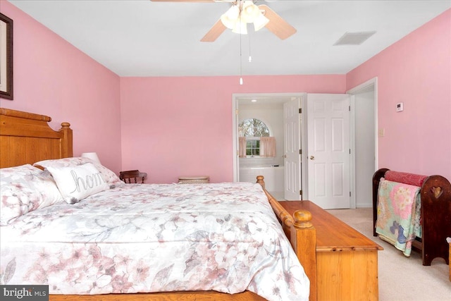 bedroom with ceiling fan, light colored carpet, and ensuite bath