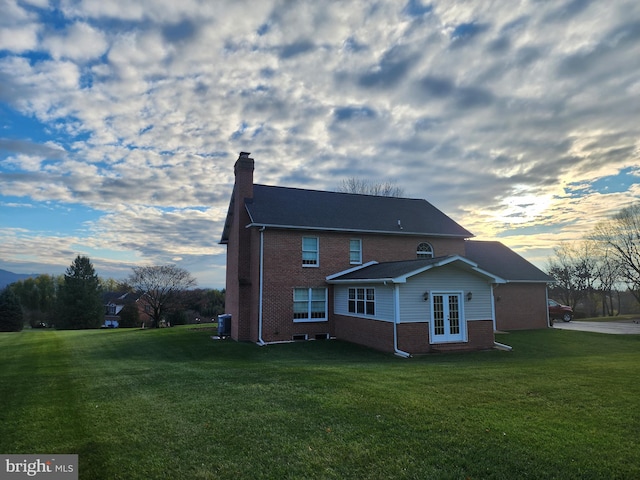 back house at dusk featuring french doors, a yard, and central AC