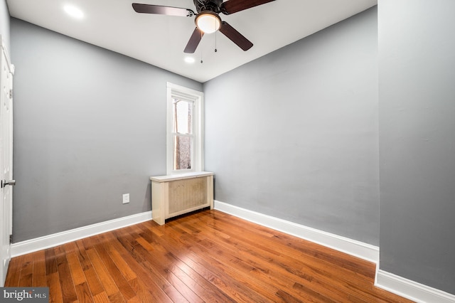 unfurnished room with hardwood / wood-style floors, ceiling fan, and radiator heating unit