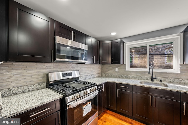 kitchen featuring sink, decorative backsplash, light wood-type flooring, appliances with stainless steel finishes, and light stone counters