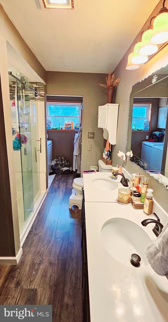 bathroom with washer and clothes dryer, vanity, a shower with door, hardwood / wood-style flooring, and toilet