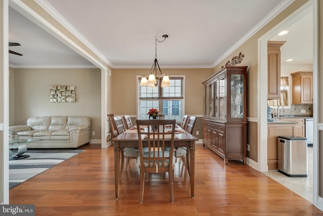 dining space featuring ceiling fan with notable chandelier, light hardwood / wood-style flooring, crown molding, and sink