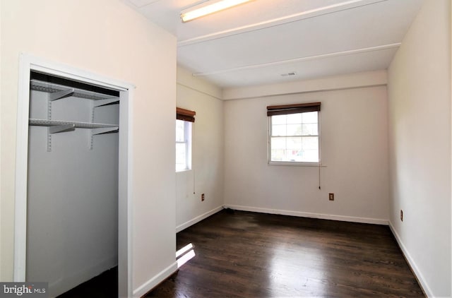 unfurnished bedroom featuring multiple windows, a closet, and dark hardwood / wood-style floors