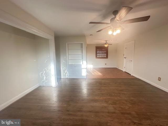 unfurnished room with ceiling fan, built in features, and dark wood-type flooring