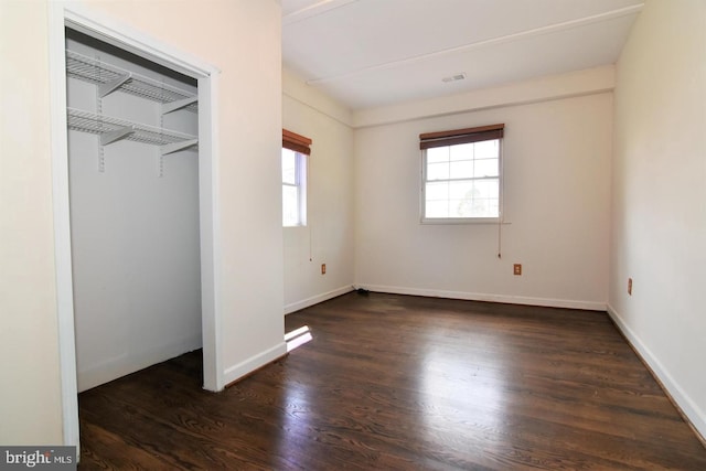 unfurnished bedroom with multiple windows, a closet, and dark hardwood / wood-style flooring