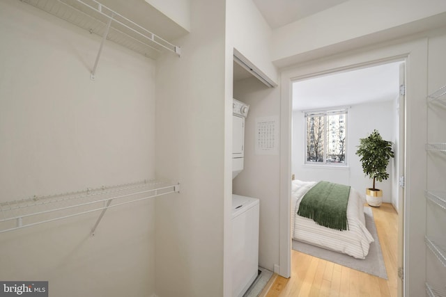 walk in closet with stacked washer / drying machine and light wood-type flooring