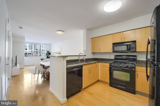 kitchen featuring kitchen peninsula, dark stone counters, black appliances, light hardwood / wood-style flooring, and sink