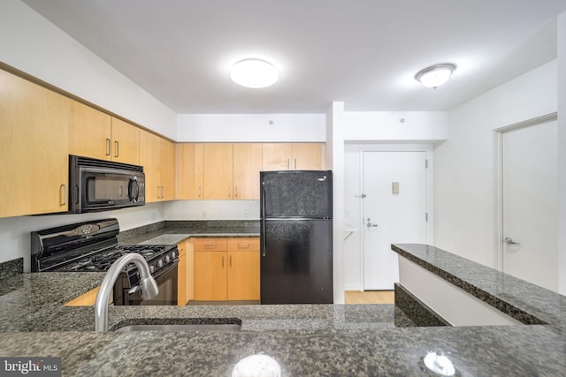 kitchen featuring light brown cabinetry, sink, black appliances, and dark stone countertops