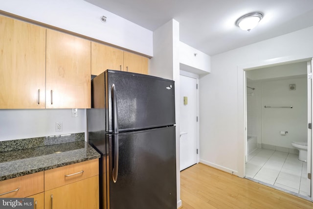 kitchen featuring light hardwood / wood-style flooring, black fridge, and dark stone countertops