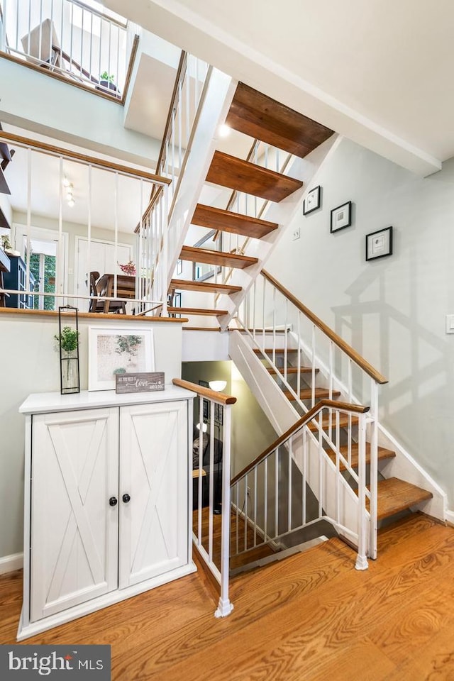 stairway with hardwood / wood-style floors and beam ceiling