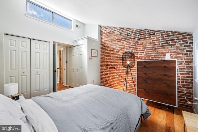 bedroom with brick wall, wood-type flooring, high vaulted ceiling, and two closets