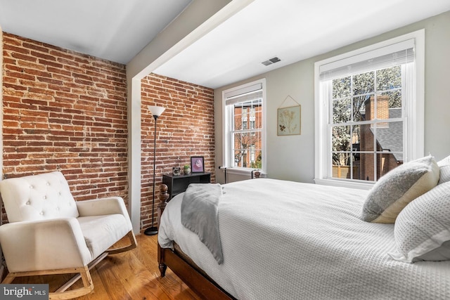 bedroom featuring hardwood / wood-style flooring, multiple windows, and brick wall