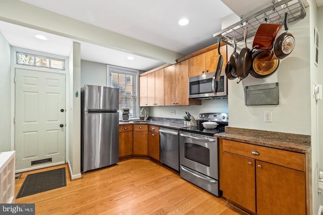 kitchen featuring dark stone countertops, sink, light wood-type flooring, and stainless steel appliances