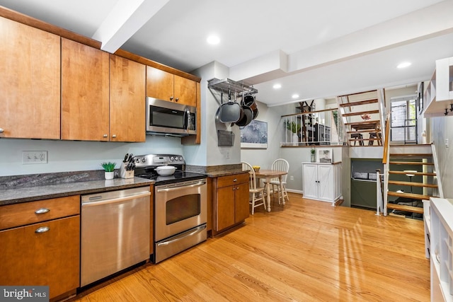 kitchen featuring beamed ceiling, dark stone countertops, stainless steel appliances, and light hardwood / wood-style flooring