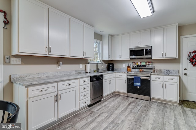 kitchen with appliances with stainless steel finishes, light wood-type flooring, white cabinetry, and sink