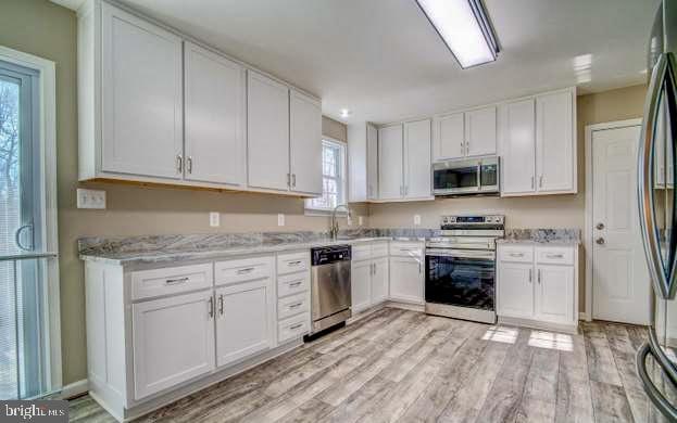 kitchen featuring white cabinetry, sink, stainless steel appliances, light stone counters, and light wood-type flooring