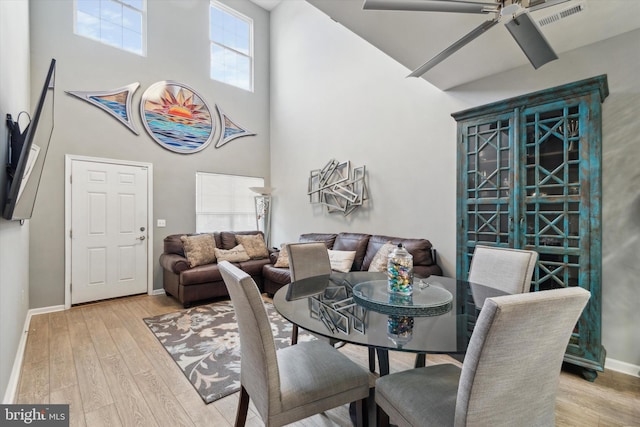 dining room featuring a towering ceiling, light wood-type flooring, and ceiling fan