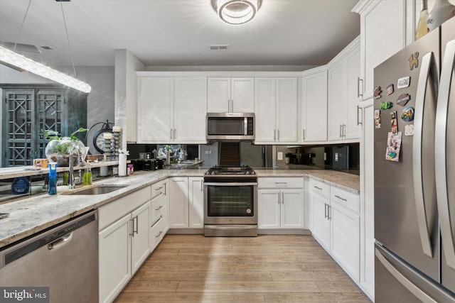 kitchen with light stone counters, white cabinets, stainless steel appliances, and light wood-type flooring