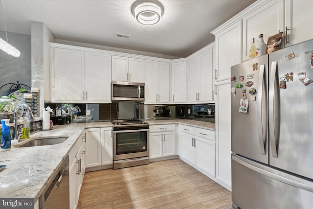 kitchen with light stone countertops, appliances with stainless steel finishes, light wood-type flooring, sink, and white cabinetry