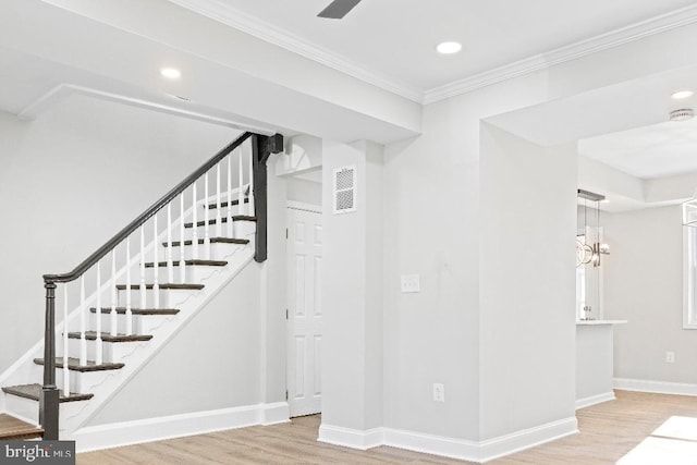 staircase with a notable chandelier, hardwood / wood-style floors, and ornamental molding