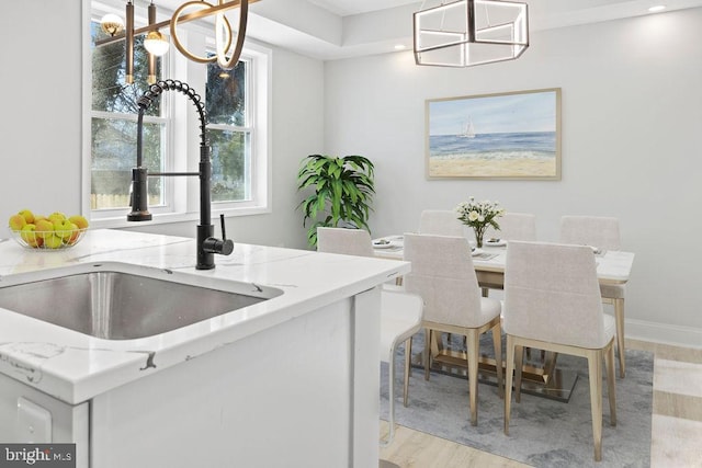 kitchen with light stone countertops, a chandelier, pendant lighting, light hardwood / wood-style floors, and sink