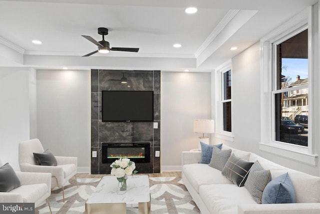 living room with a fireplace, a raised ceiling, ceiling fan, light wood-type flooring, and crown molding