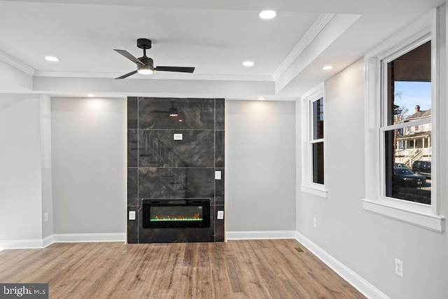 unfurnished living room featuring a raised ceiling, ceiling fan, ornamental molding, a fireplace, and hardwood / wood-style flooring