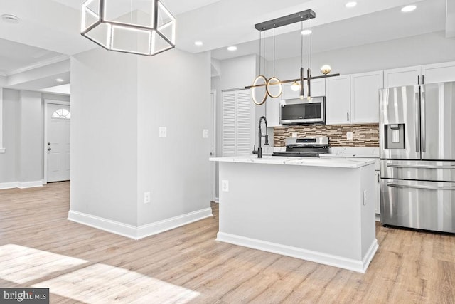 kitchen featuring stainless steel appliances, decorative light fixtures, white cabinetry, light hardwood / wood-style floors, and an island with sink