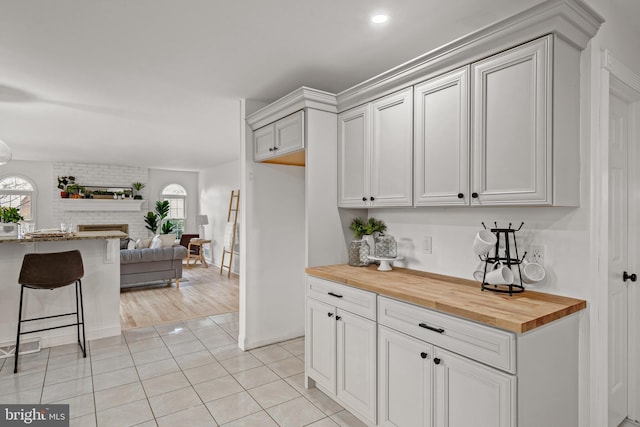 kitchen with wood counters, a kitchen breakfast bar, a fireplace, light hardwood / wood-style floors, and white cabinetry