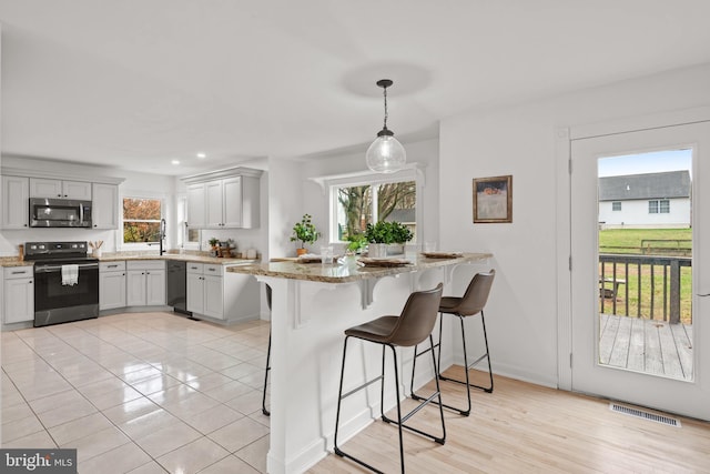 kitchen featuring light stone countertops, kitchen peninsula, light wood-type flooring, black appliances, and hanging light fixtures