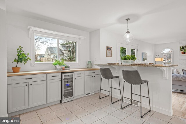 kitchen featuring a kitchen bar, hanging light fixtures, beverage cooler, and light wood-type flooring