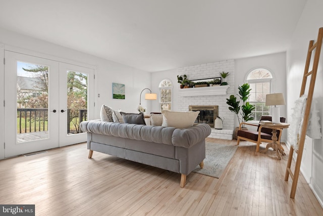 living room with french doors, light hardwood / wood-style floors, and a brick fireplace