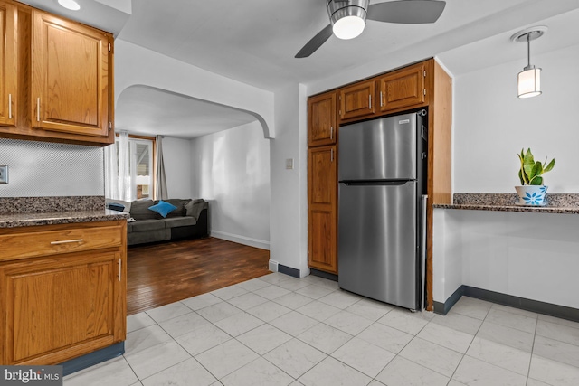 kitchen with stainless steel refrigerator, hanging light fixtures, dark stone counters, and ceiling fan