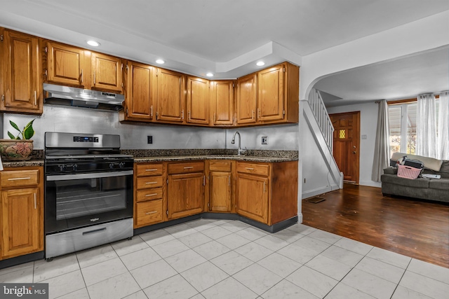 kitchen featuring decorative backsplash, dark stone counters, stainless steel gas range, sink, and light hardwood / wood-style flooring