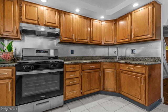 kitchen with stainless steel gas stove, sink, dark stone counters, decorative backsplash, and light tile patterned flooring