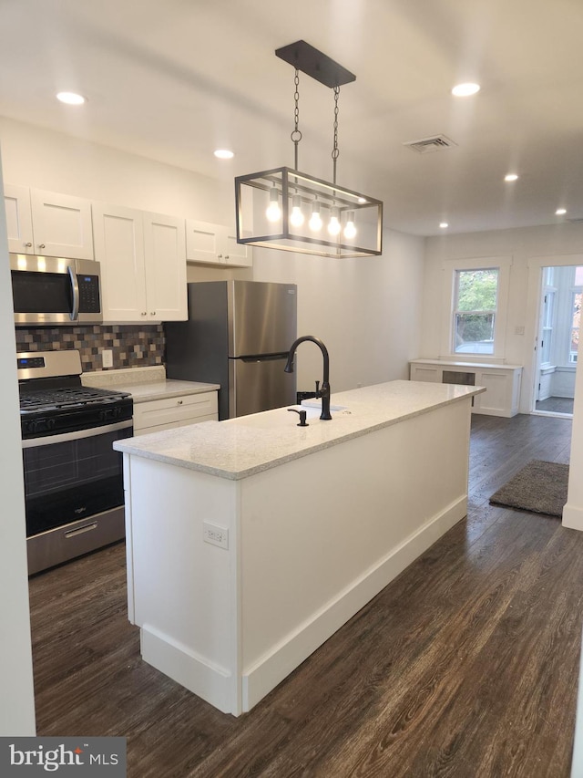 kitchen with a kitchen island with sink, white cabinets, pendant lighting, and appliances with stainless steel finishes